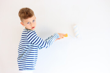 A young boy renovating a room, sanding the walls with sandpaper and painting them white with a...