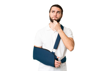 Young handsome man with broken arm and wearing a sling over isolated chroma key background having...