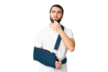 Young handsome man with broken arm and wearing a sling over isolated chroma key background having doubts and thinking