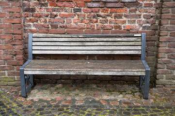 Empty wooden bench resting against weathered brick wall