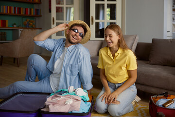 Overjoyed loving couple folding garment into travel suitcases