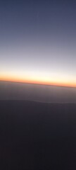 Sunset Horizon Captured from an Airplane. A mesmerizing view of the horizon at sunset, showcasing a gradient of colors from dark blue to orange, captured from an airplane window