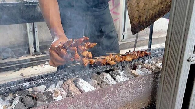 Cinematic shot. The traditonal serving process of lamb satay grilled on burning charcoal and fire. Asian street culinary concept.