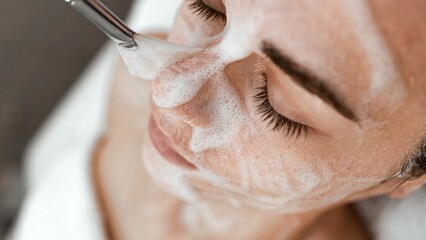 Female beautician applying cleansing foam on woman face. Cosmetology procedure in beauty clinic. Anti-age procedure. Morning or evening beauty routine. Perfect skin concept. 