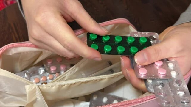 Sorting through a home first aid kit, examining medicine packages in a close-up view.