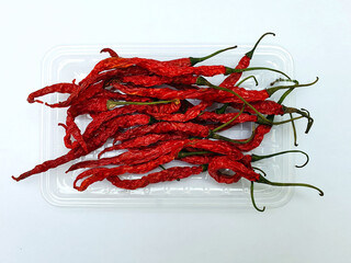 Pile of dried red chilies or chilli cayenne pepper on clear plastic tray isolated on white background.