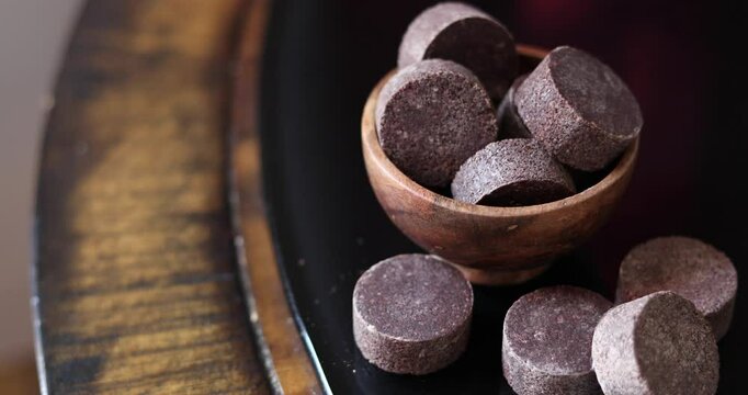 Close-up view of a small, dark-brown wooden bowl filled with several irregularly shaped pieces of dark, possibly chocolate-like material. 