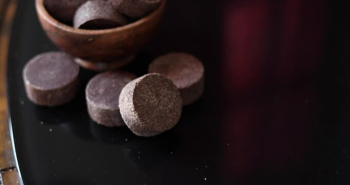 Close-up view of a small, dark-brown wooden bowl filled with several irregularly shaped pieces of dark, possibly chocolate-like material. 