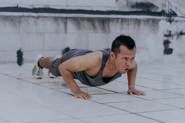Photo of asian man doing push-ups during a fitness session on the terrace of his home. Fitness, sport, training and lifestyle concept.