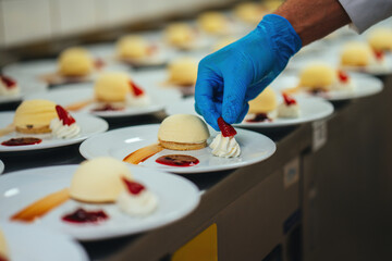 A chef is preparing a cake plate for a special occasion. The chef is putting strawberries on top of the whipped cream.