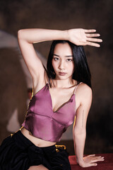 Asian woman sitting elegantly on vintage red sofa in chic stage outfit