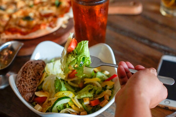 Person eating a bowl of vegetables salad with a fork