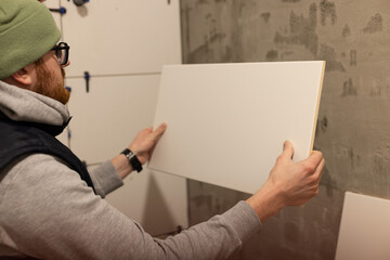 Man tiling bathroom walls with white ceramic tile.