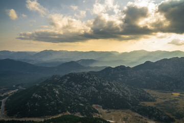 An impressive sunrise skyscape in the early morning. Yellow sun rays filter through the clouds towards the mountains and the ground.