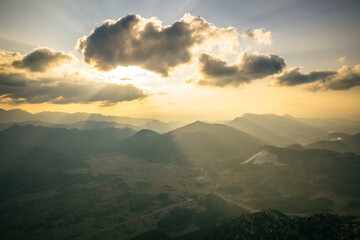Obraz premium Dramatic sky with yellow sun rays streaming through the clouds onto the mountains at sunrise in the early morning.