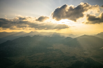 Dramatic sky with yellow sun rays streaming through the clouds onto the mountains at sunrise in the early morning.