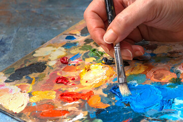 Artist's hands with old used brushes in an artist's studio, palette with multi-colored spots of oil...
