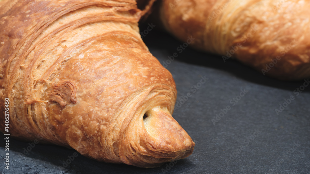 Poster a croissant with a hole in the middle. it is on a black surface. the croissant is brown and has a sl