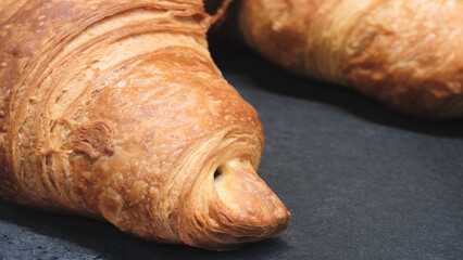 A croissant with a hole in the middle. It is on a black surface. The croissant is brown and has a slightly crispy texture