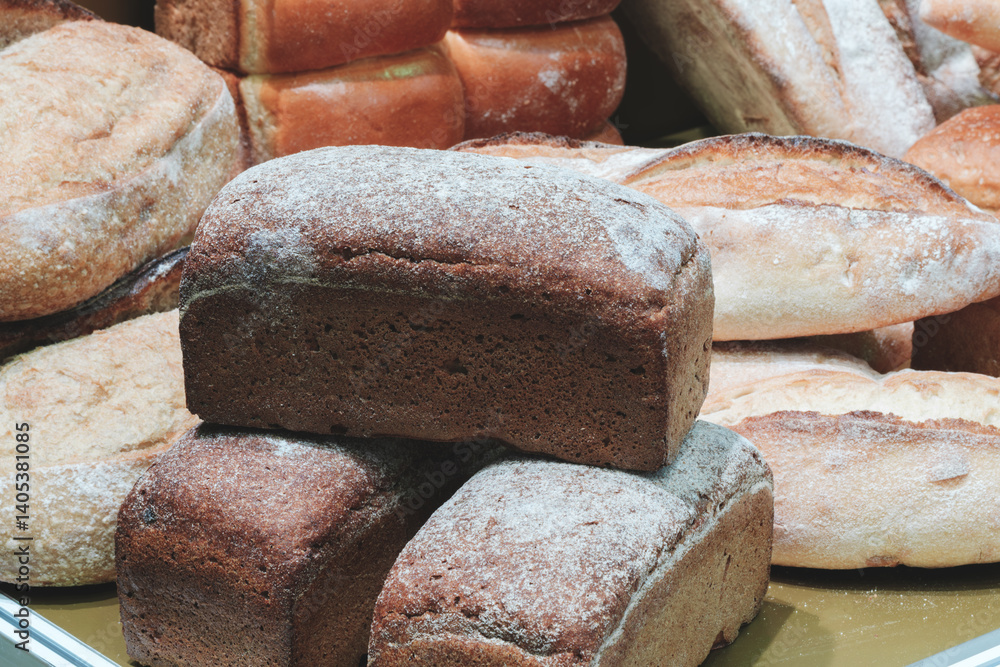Poster a stack of bread with a white powder on top. there are many other loaves of bread in the background