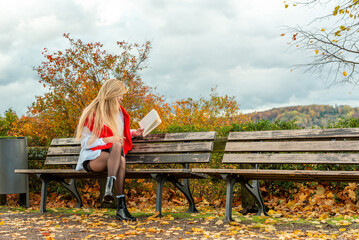 Woman with long hair reads a book on a park bench in an autumn scenery