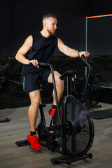 Obraz premium Shirtless athletic man training on air bike at modern gym..