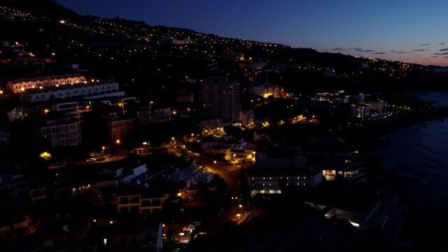 Night Aerial View of Canico de Baixo, Coastal Town with warm illumination on a hillside in Portugal
