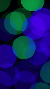 Una toma de cerca de varias luces de colores en forma de c&iacute;rculos en movimiento en la oscuridad. Desenfoque, efecto Bokeh. Video vertical.