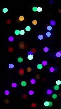Una toma de cerca de varias luces de colores en forma de c&iacute;rculos en movimiento en la oscuridad. Desenfoque, efecto Bokeh. Video vertical.