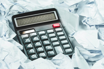Black calculator with crumpled sheets of paper.