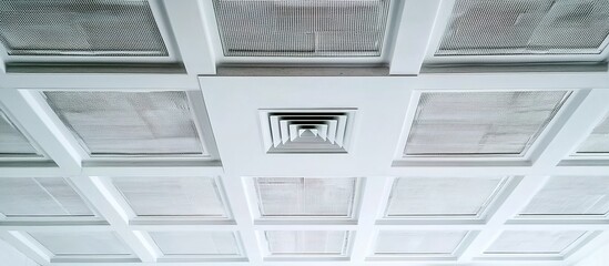 Obraz premium Ceiling grid of square white air vents in precise alignment, central circular ventilation unit with radial blades, sterile hospital lighting creating geometric shadow patterns.