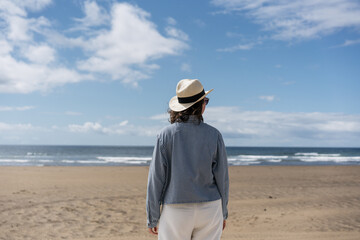 Solo traveller woman in a straw hat standing back to camera and looking at the sea