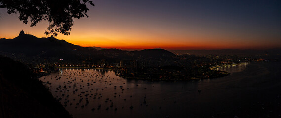 Panoramic night aerial view of Guanabara Bay and mountains of Rio de Janeiro and Christ the Redeemer in the background, coast of Brazil.