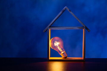 Light bulb glowing in house made by wooden on blue background. House model and light bulb, power...