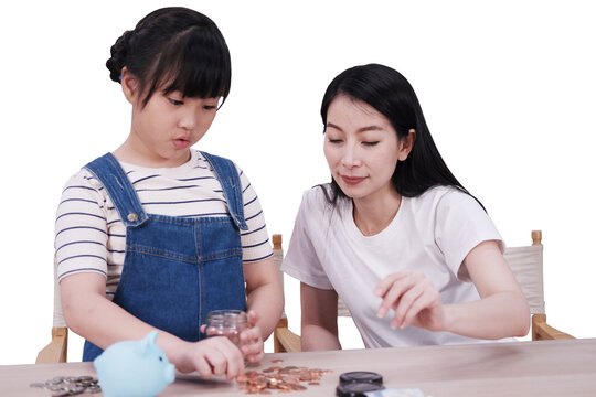 Smiling Asian daughter and mother putting coins into piggy bank for saving money for the future on wooden table. Child educational for homeschooling concept