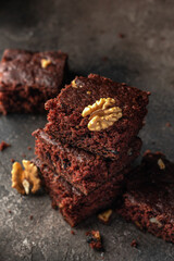 Stack of delicious brownie pieces with hazelnuts on top on dark background close up