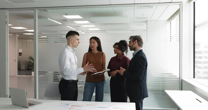 Multinational young and middle-aged teammates, company employees participating in team discussion or debriefing after training or formal meeting event in modern conference room. Business communication