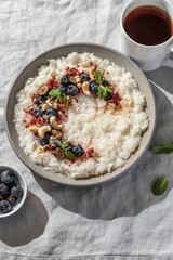 Rice porridge with blueberries, dried raspberries and nuts on a linen tablecloth, hot and healthy breakfast with tea. Bright morning light