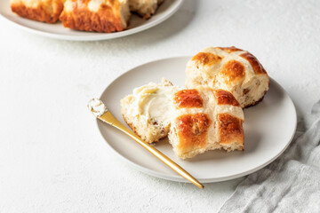 Traditional Easter hot cross buns on white plate with butter on white background. Delicious Easter breakfast