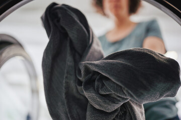Inside view of washing machine as woman loads dark fabric at laundromat
