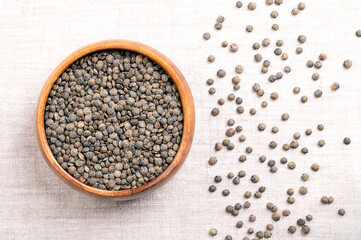 Puy lentils in a wooden bowl on linen. Dried variety of small lentils, mottled, of slate-gray to dark green color, with blue marbling. Lens esculenta variety, grown in the Auvergne region of France.