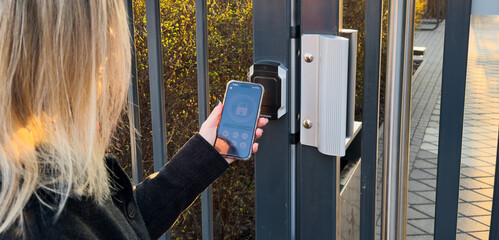 Woman locking smartlock on the entrance door using a smart phone. Concept of using smart electronic locks with keyless access.