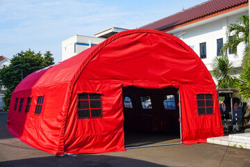 A large red tent stands on pavement, likely for social services or disaster relief purposes Use for...