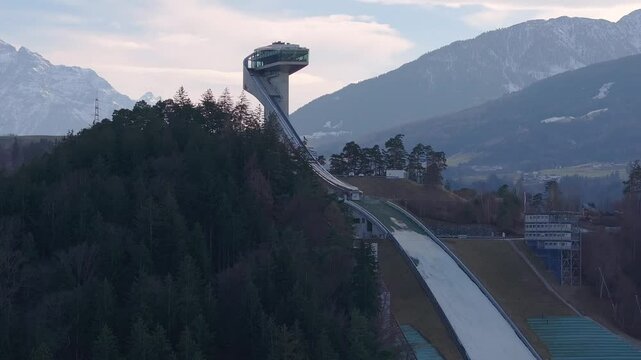 Aerial view of the Bergisel Ski Jump in Innsbruck, Austria, with gradual motion showcasing its modern design and the surrounding snow capped Alps.