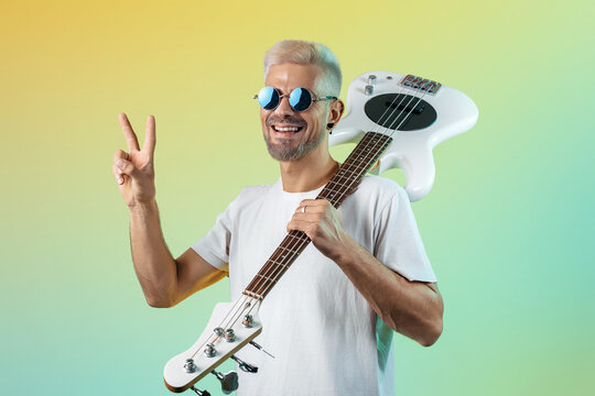 Handsome hipster man play white bass guitar in neon lights. Rock music concept. Peace gesture