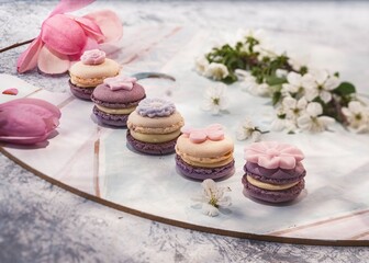 Colorful macarons in various pastel shades are artfully placed on a decorative plate. Seasonal flowers and petals surround the treats, creating a delightful spring atmosphere that enchants the senses
