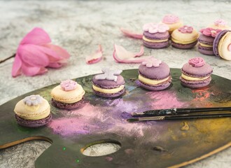 Colorful macarons sit elegantly on a painter's palette, showcasing shades of purple and cream,...