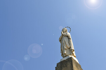 Low-angle view of a statue of the Virgin Mary against blue sky, with lens flares