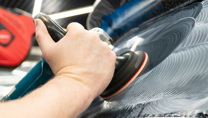 Obraz premium A man polishes the glass of a car with a polishing machine from small scratches with a large one. Auto glass repair, replacement. Car detailing. Hands with an orbital polishing machine. Close-up.