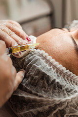 Young woman recieving injection of anti-aging botox filler to forehead from professional cosmetologist in beauty salon